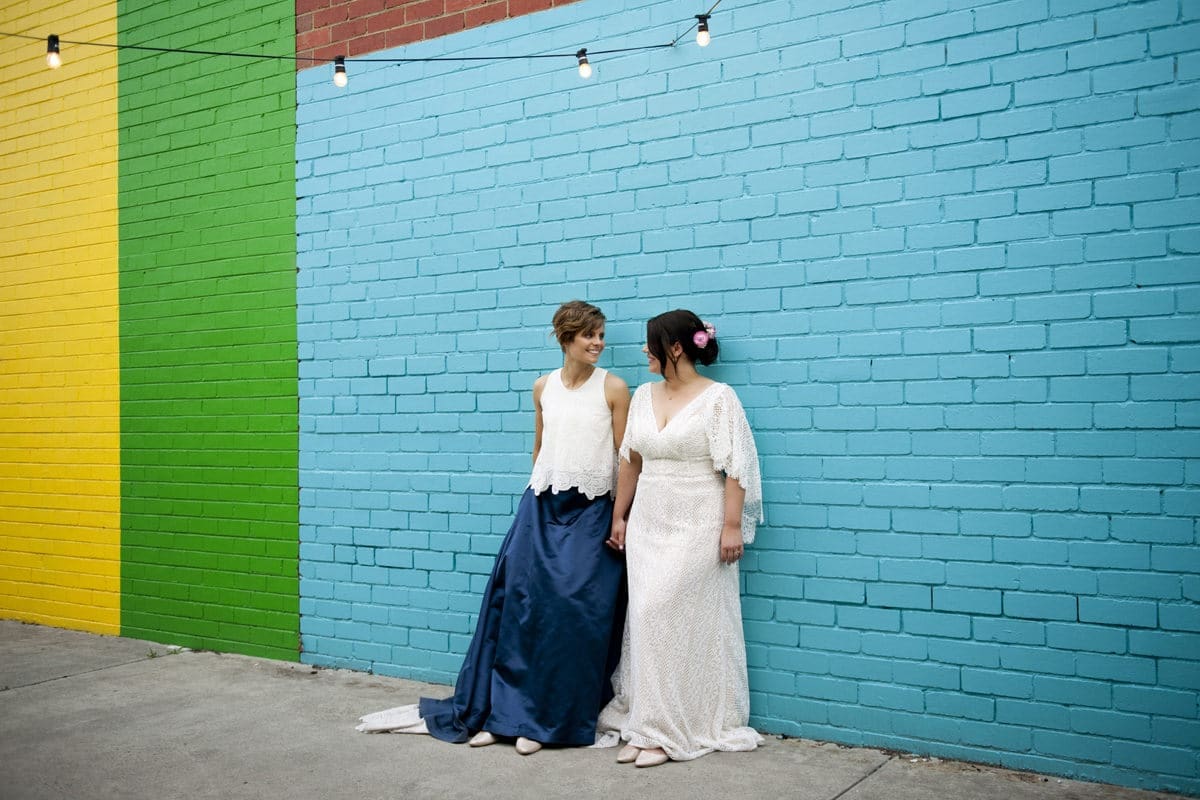 Two Brides Pose Against Colourful Wall In Melbourne Wedding Photographed by Natalie Davies